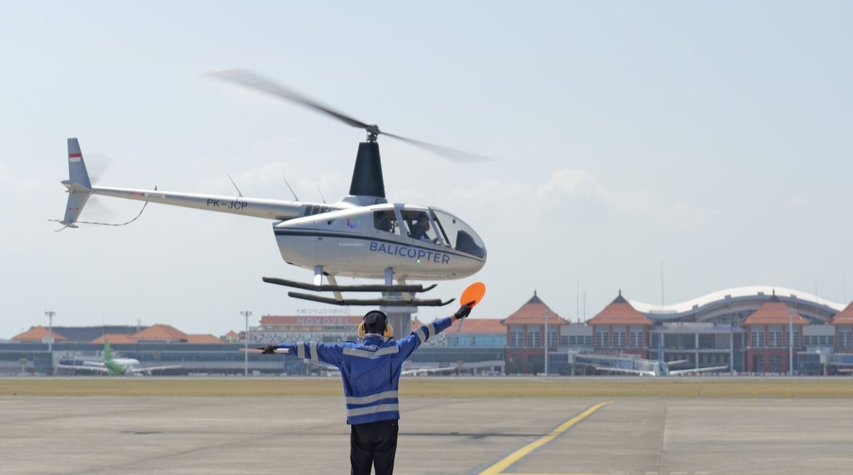 A helicopter landing on the apron at Ngurah Rai International Airport, guided in by a licensed landing officer